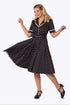 A woman modeling a black and white polka dot midi dress with white trim, posed in a dynamic twirling stance against a plain white studio background.